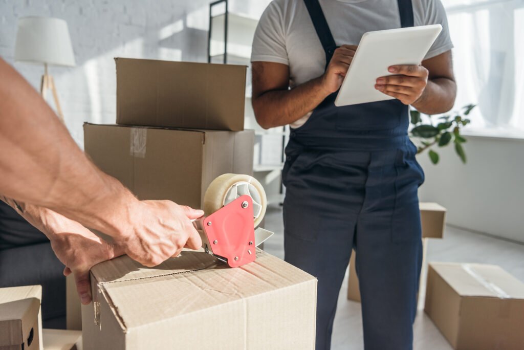 Kenner Moving Services team providing professional packing services, securing boxes with tape and using a checklist for an organized and efficient move