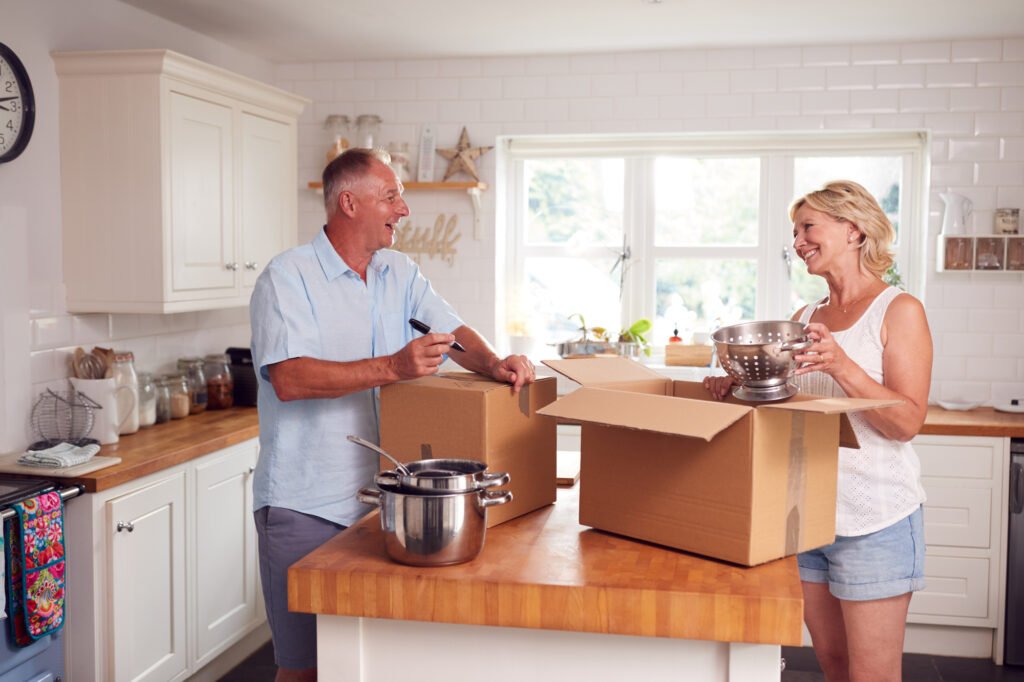 Couple packing kitchen items into boxes; contact us at Kenner Moving Services for expert packing and moving solutions tailored to your needs.